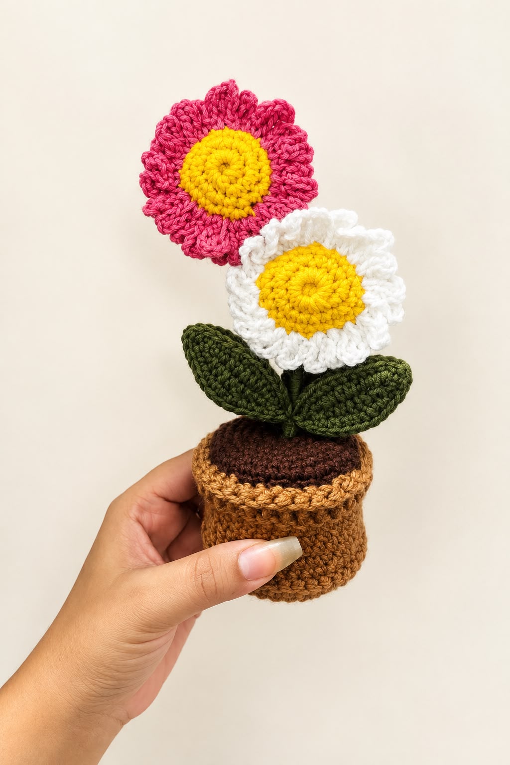 Blush Daisy Duo Pot held in a hand, showing the pink and white crochet daisies and pot